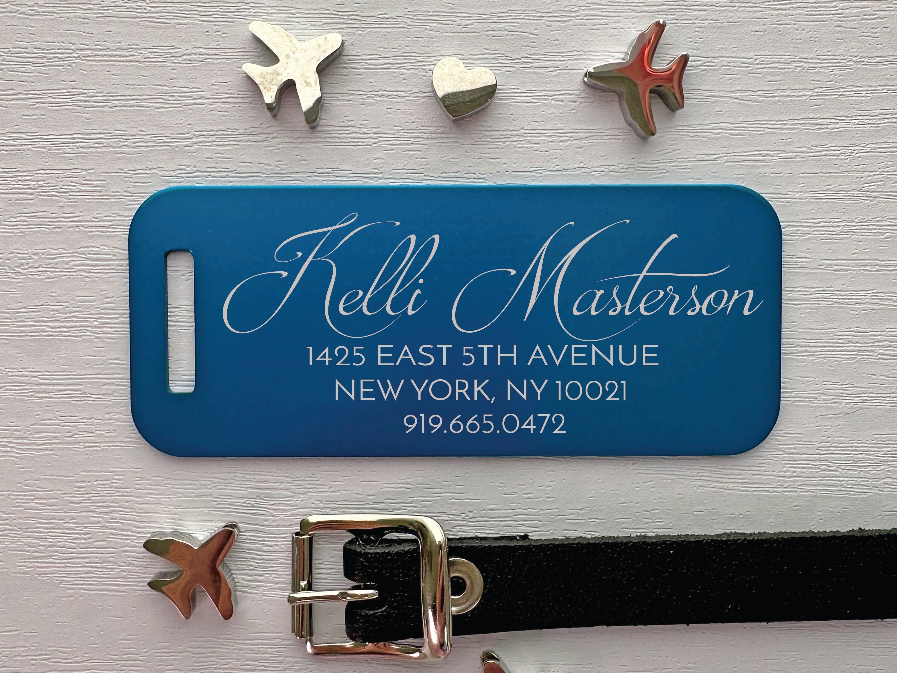 Blue luggage tag with white text on a light gray background with decorative items.
