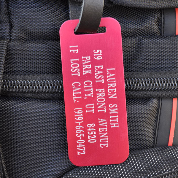 Personalized red aluminum luggage tag with black leather strap on suitcase