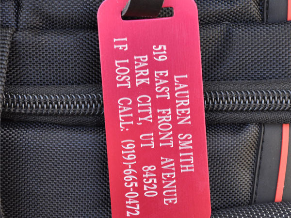 Custom engraved red aluminum luggage tag with leather strap, ideal for identifying travel bags, backpacks, or checked gear.