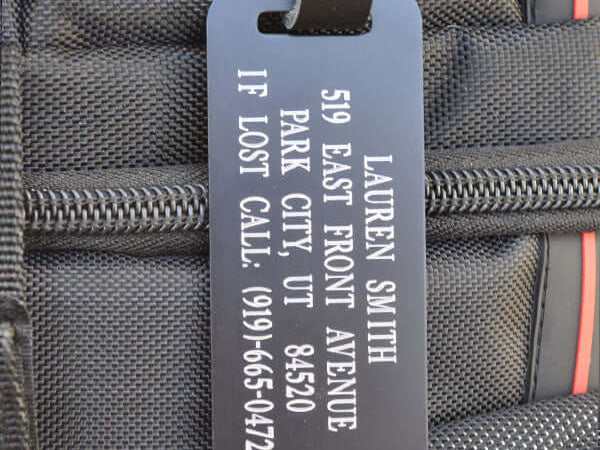 Custom engraved black aluminum luggage tag with silver lettering and leather strap