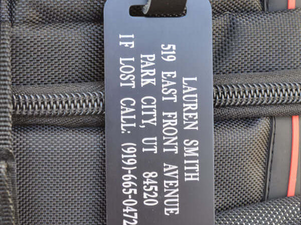 Custom engraved black aluminum luggage tag with silver lettering and leather strap
