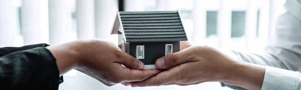 Two hands exchanging a miniature house model, symbolizing real estate ownership transfer.