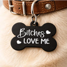 Black bone-shaped dog ID tag reading “Bitches Love Me” attached to a leather dog collar